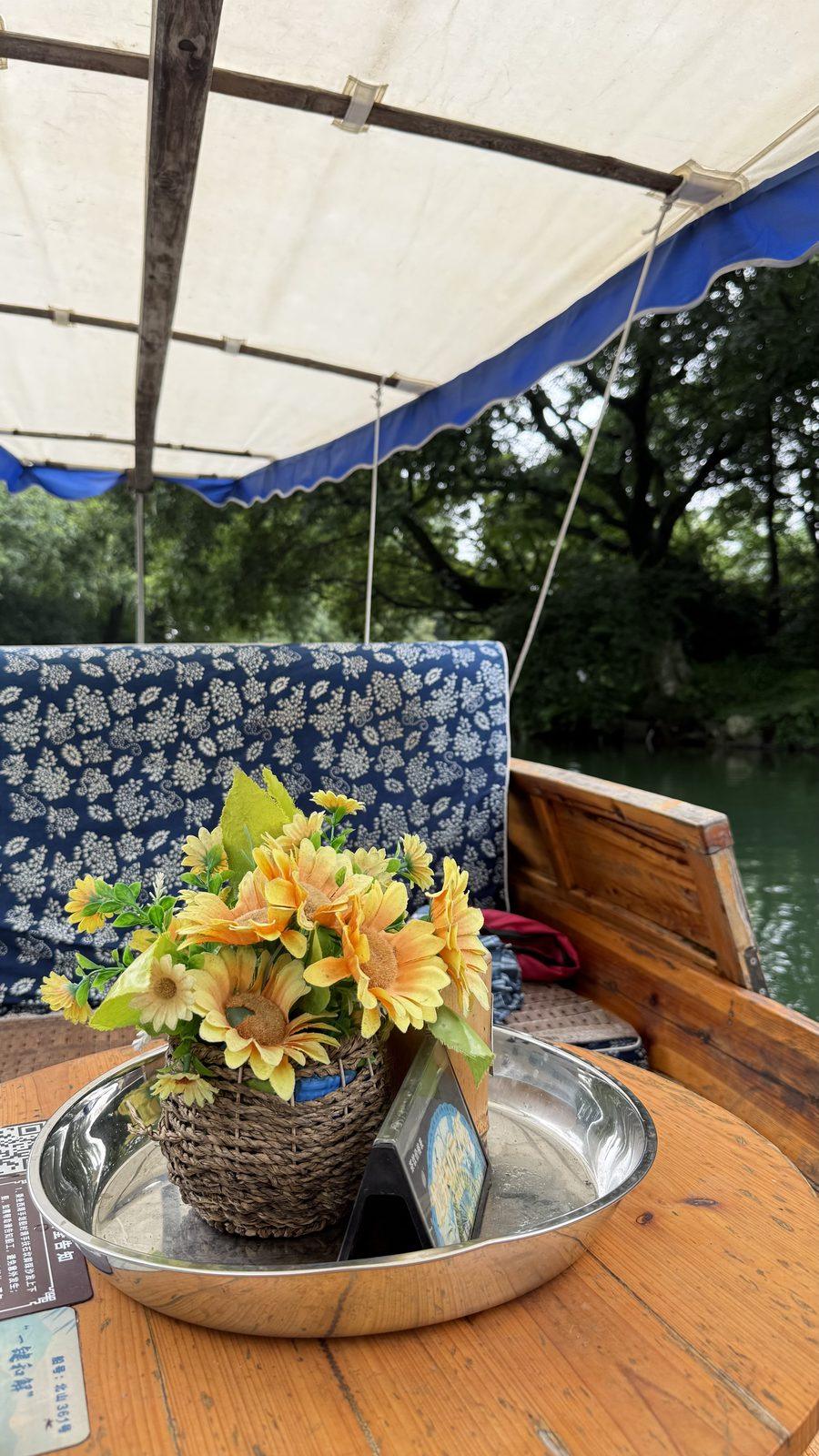 A small table with flowers under the canopy of a hand-rowed boat on West Lake, Hangzhou