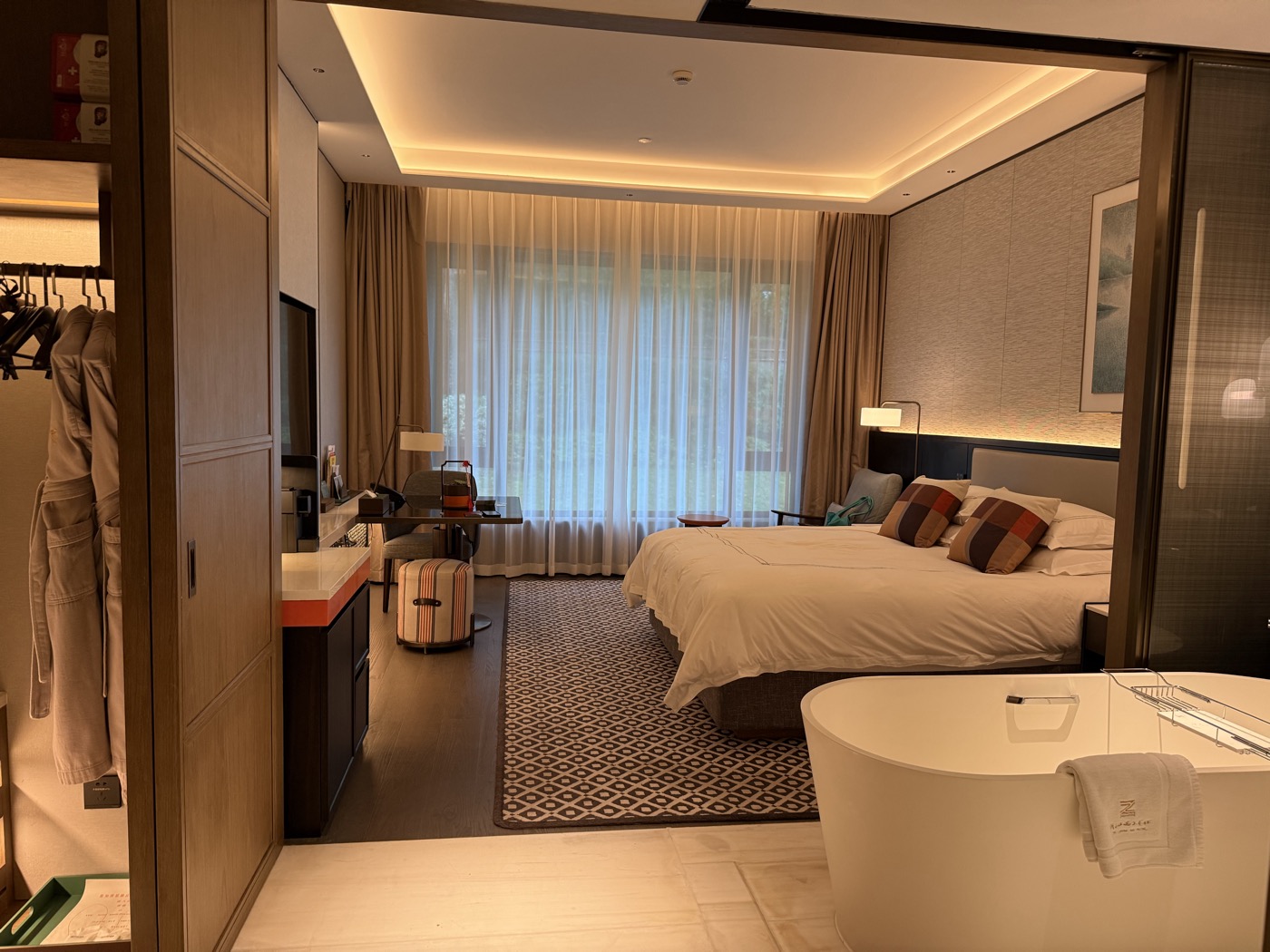A hotel room with a large bed and a freestanding bath beside floor-to-ceiling windows